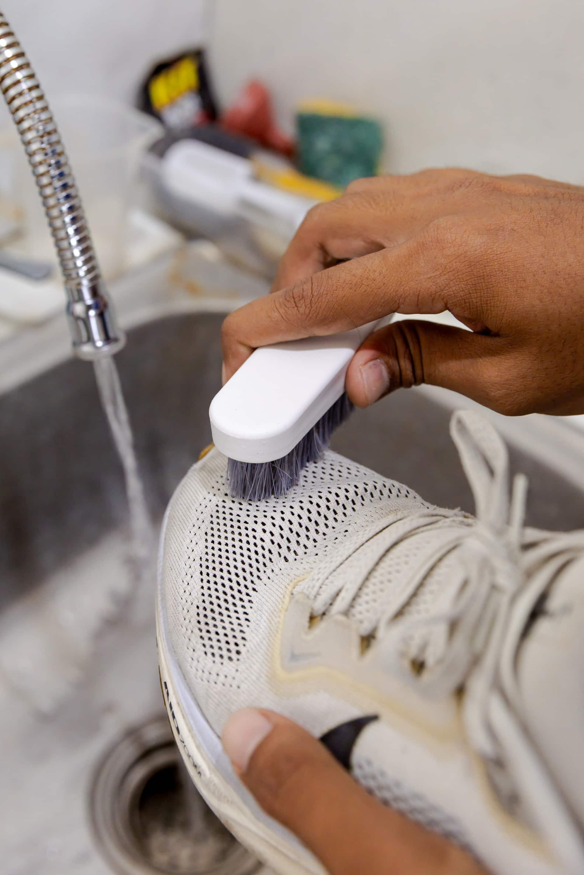 Easy Day Laundry team member hand-brushing a white knit sneaker at the wash sink