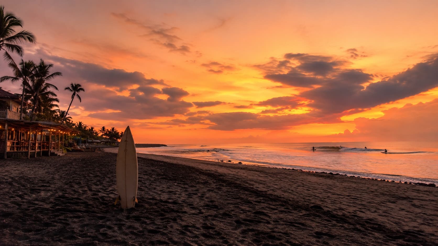 Echo Beach Canggu at sunset with surfers in the lineup and beach bars on the sand