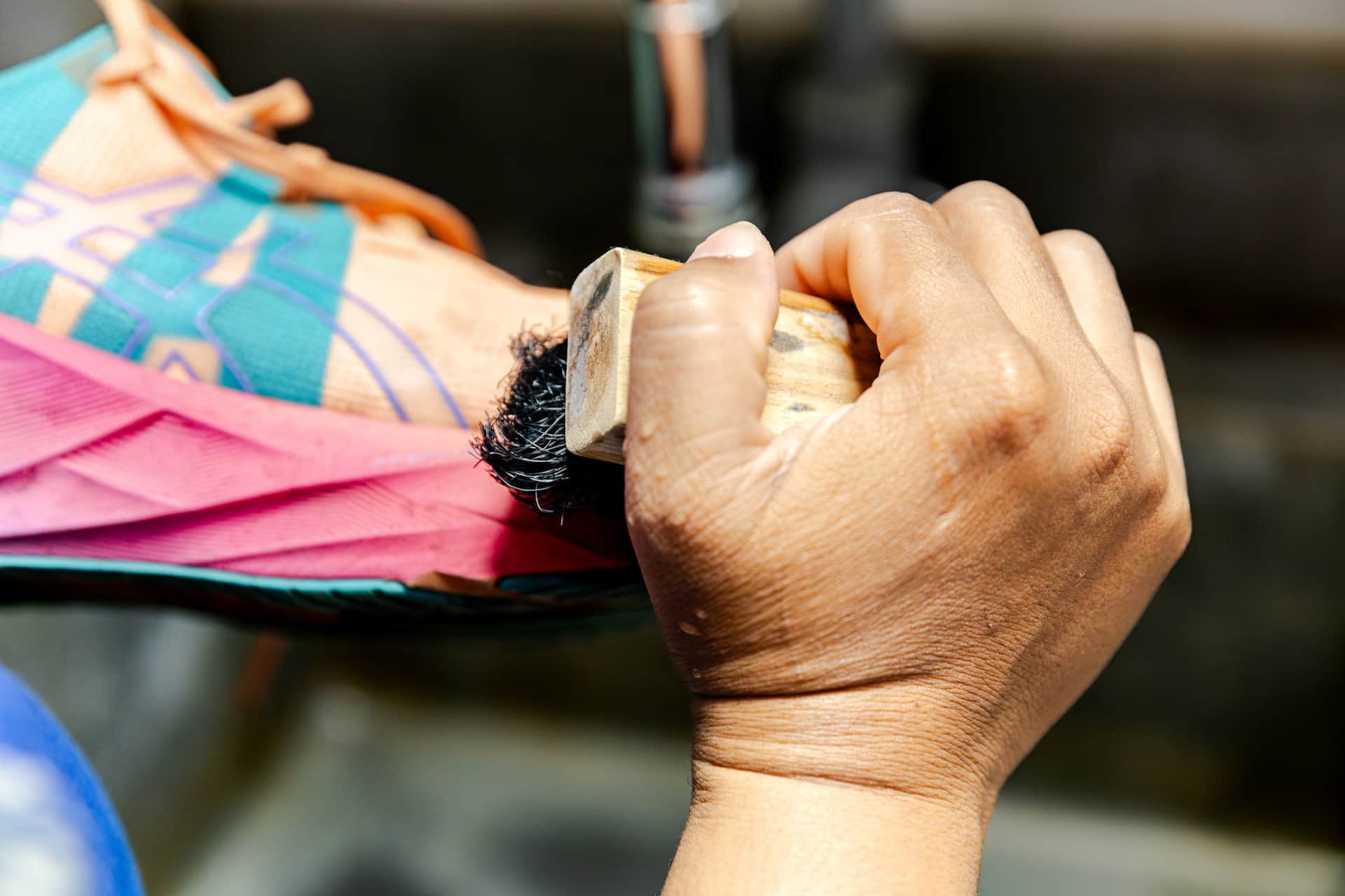 Close-up of a running shoe being hand-scrubbed with a wooden brush